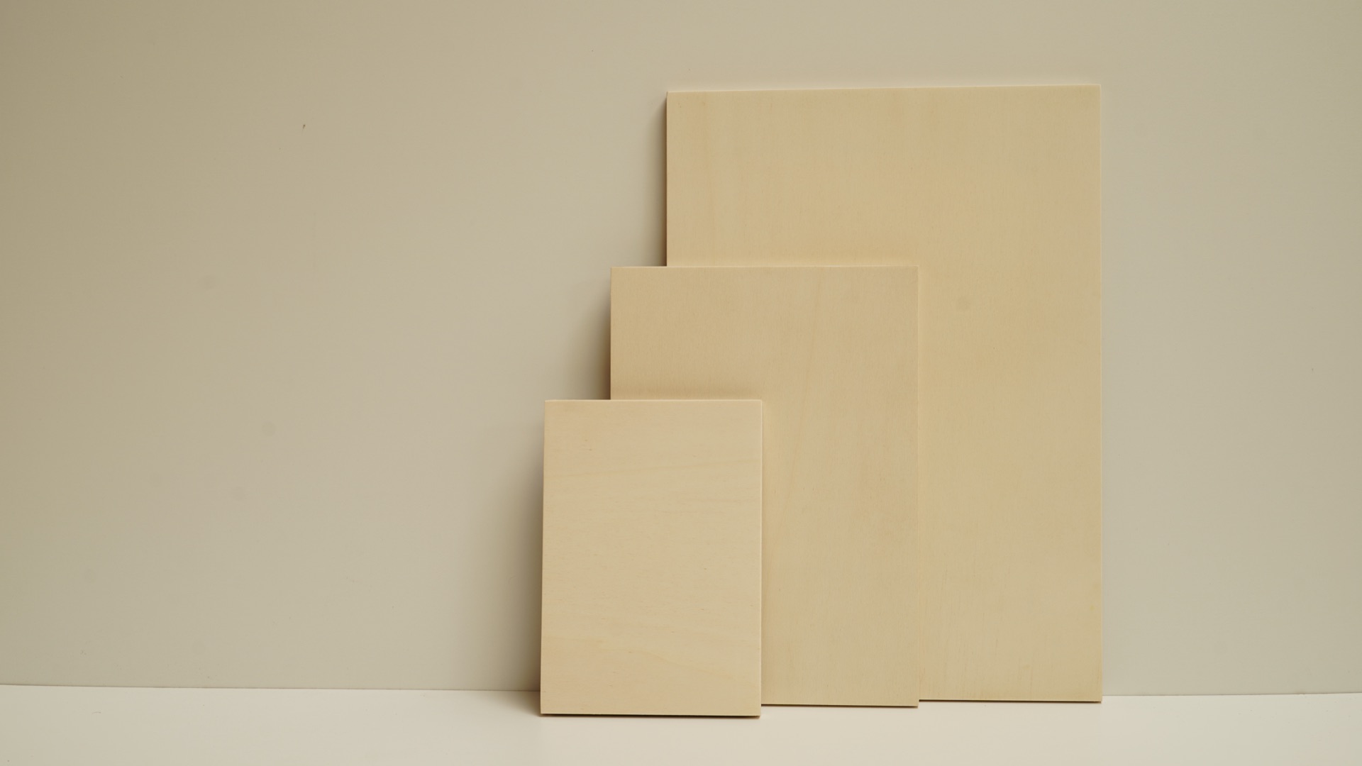 Three blank light maple plywood art boards leaning against a wall in stepped sizes